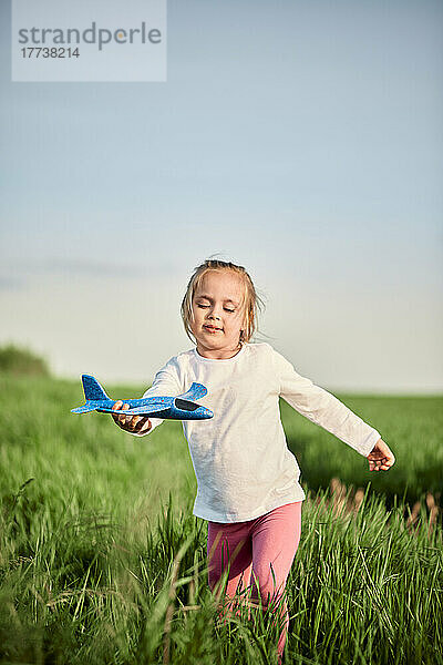Nettes Mädchen mit Flugzeugmodell  das auf einer Wiese läuft