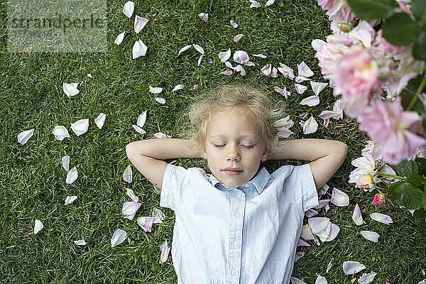Nettes Mädchen mit geschlossenen Augen liegt auf Gras im Rosengarten