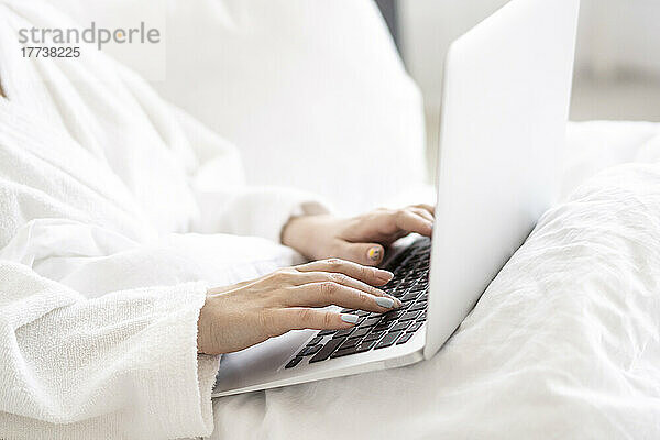 Frau sitzt mit Laptop zu Hause im Bett