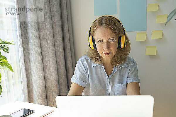 Reife Geschäftsfrau mit kabellosen Kopfhörern und Laptop  die im Heimbüro arbeitet