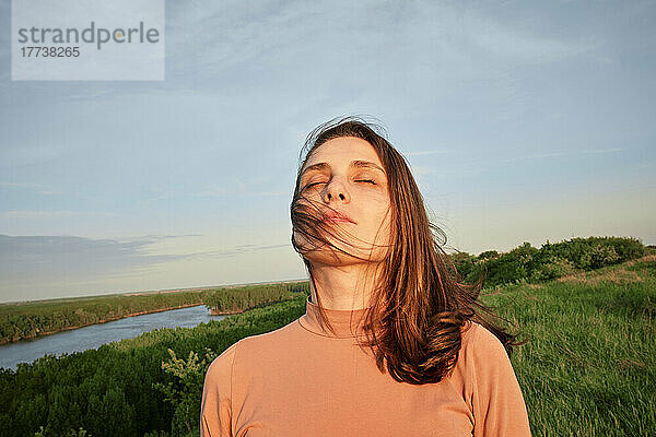 Junge Frau mit geschlossenen Augen im Sonnenlicht auf einem landwirtschaftlichen Feld