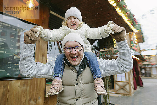 Glücklicher Vater trägt Tochter auf Schultern auf dem Weihnachtsmarkt