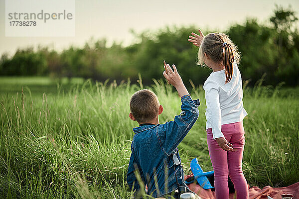 Bruder und Schwester winken auf dem Feld mit den Händen