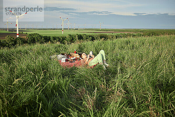 Frau liest Buch und liegt auf Picknickdecke im Feld