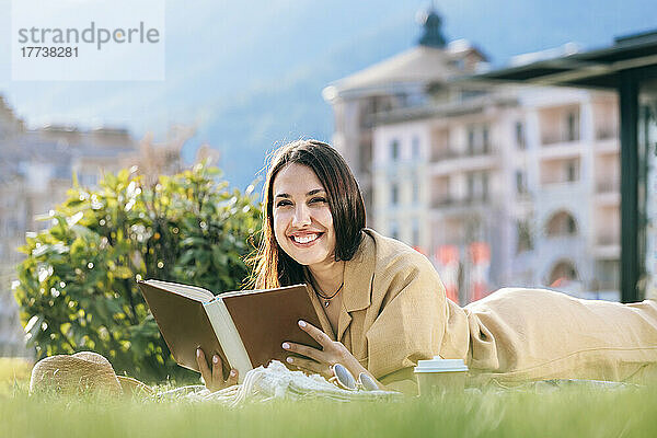 Glückliche Frau mit Buch  die an einem sonnigen Tag im Park liegt