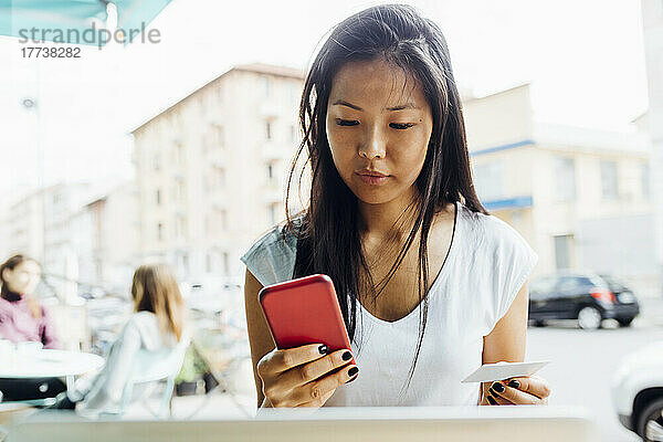 Junge Frau mit Kreditkarte beim Online-Shopping per Smartphone sitzt im Straßencafé