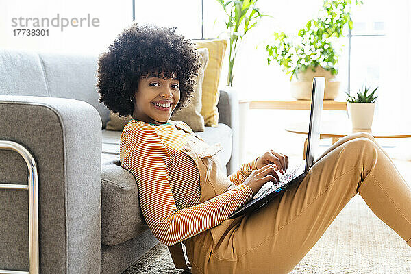 Lächelnde Frau mit Laptop  die zu Hause auf dem Sofa lehnt