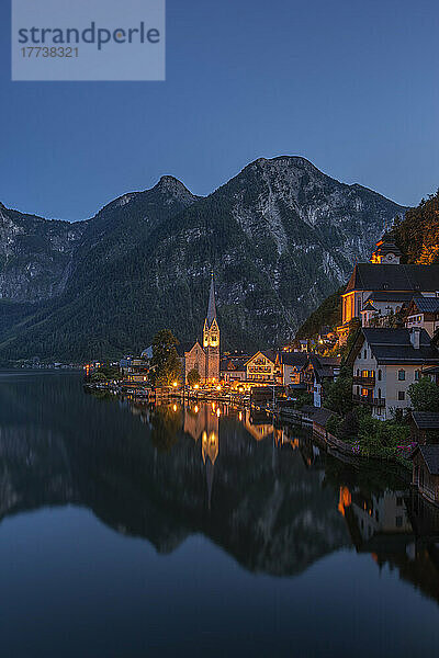 Österreich  Oberösterreich  Hallstatt  Blick auf die Stadt am Seeufer in der Abenddämmerung mit beleuchteter Kirche im Hintergrund