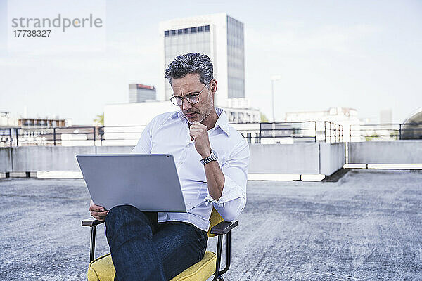 Geschäftsmann mit Brille und Laptop sitzt auf der Terrasse des Gebäudes