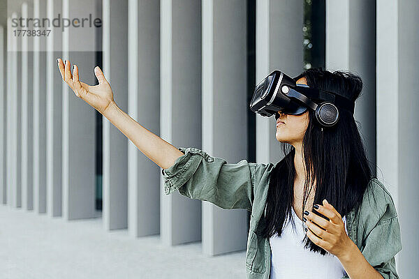Junge Frau mit Virtual-Reality-Simulator gestikuliert vor der Säule