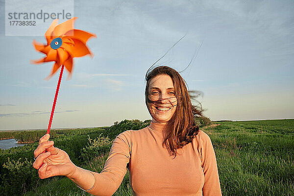 Glückliche Frau hält am Wochenende ein Windradspielzeug auf der Wiese