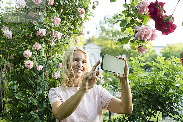 Glückliche Frau macht Selfie per Smartphone im Rosengarten