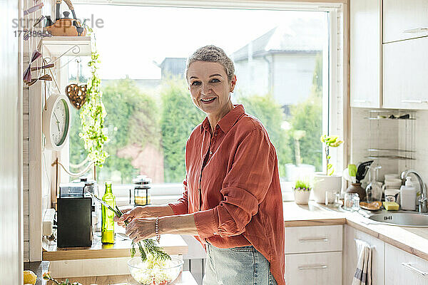 Lächelnde Frau hält Kräuter in der heimischen Küche