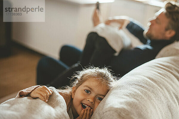 Smiling cute girl sitting by father on sofa