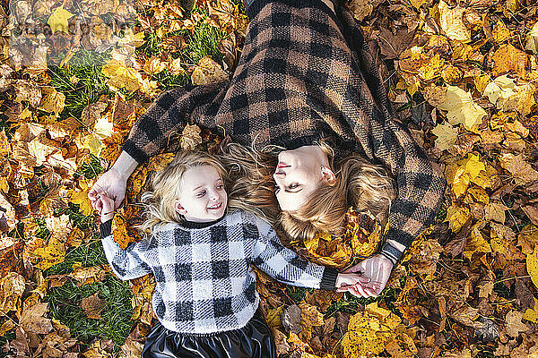 Mother and daughter lying down on autumn leaves at park