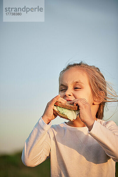 Mädchen isst Sandwich vor dem Sonnenuntergangshimmel