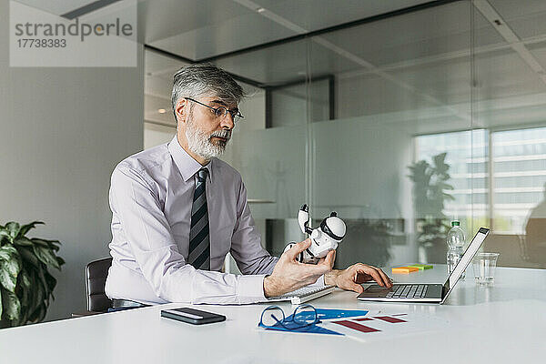 Geschäftsmann mit Spielzeugroboter sitzt am Schreibtisch im Büro