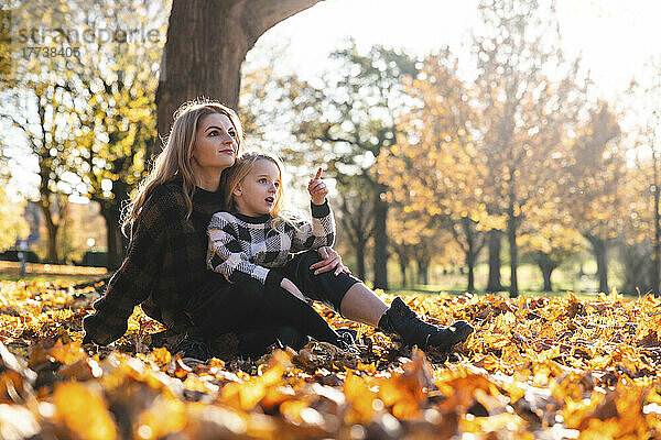 Tochter gestikuliert  während sie mit Mutter im Herbstpark sitzt