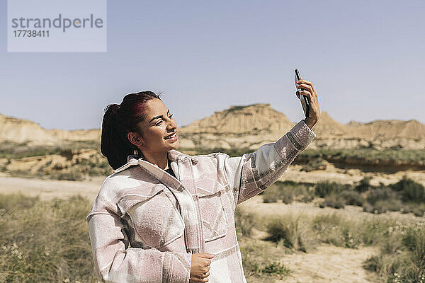 Lächelnde Frau  die an einem sonnigen Tag ein Selfie mit dem Smartphone macht