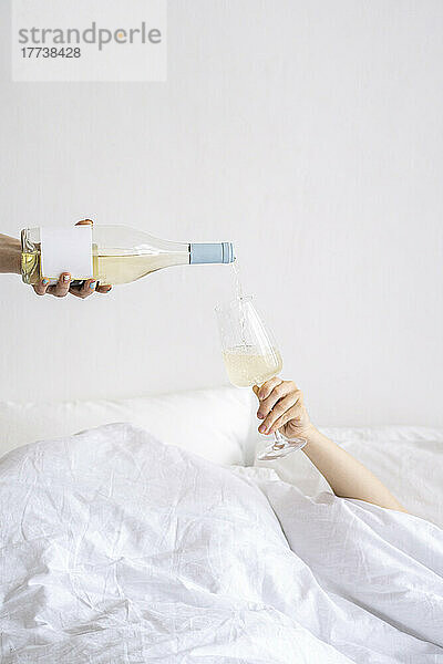 Hand gießt Wein in ein Weinglas  das zu Hause auf dem Bett gehalten wird