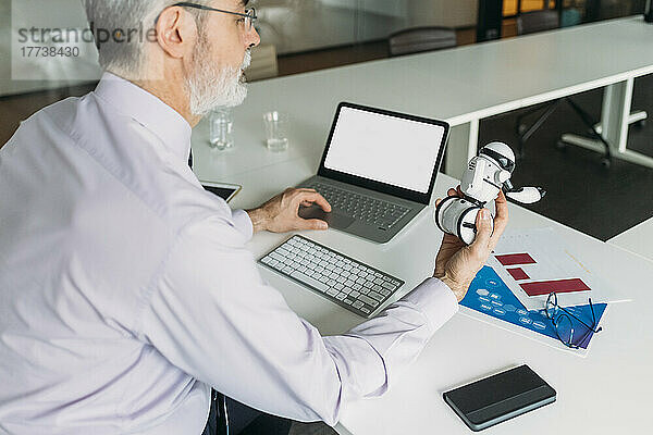 Geschäftsmann analysiert Spielzeugroboter  der am Schreibtisch im Büro sitzt