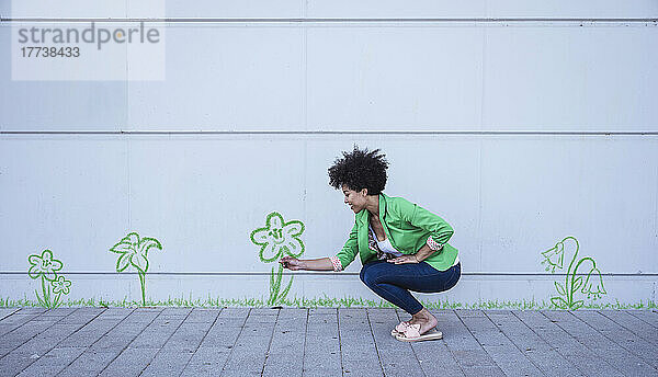 Crouching woman plucking painted flower from wall