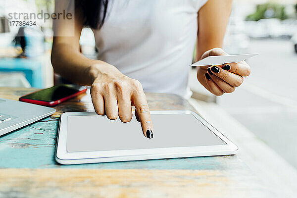 Hände einer Frau mit Kreditkarte  die im Straßencafé online über einen Tablet-PC bezahlt