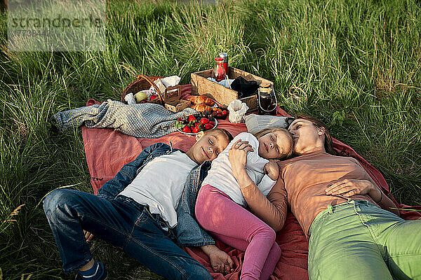 Junge Frau schläft beim Picknick neben Kindern auf dem Feld
