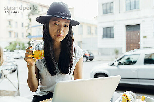 Junger Freiberufler mit einem Glas Saft und einem Laptop sitzt im Straßencafé