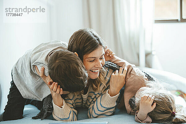 Playful mother with children lying on bed at home