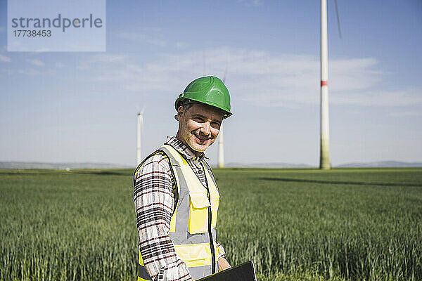 Glücklicher Ingenieur mit Schutzhelm  der auf dem Feld steht