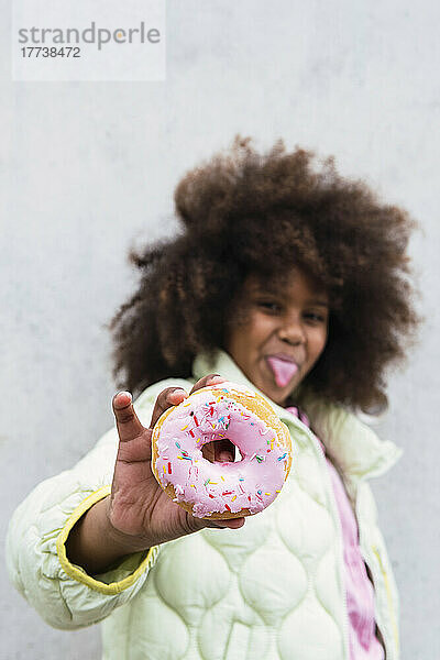 Mädchen hält Donut vor Wand