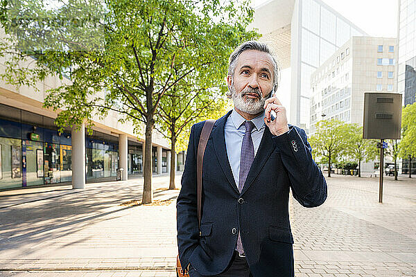 Lächelnder Geschäftsmann mit Bart  der auf dem Smartphone spricht