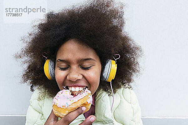 Mädchen mit Kopfhörern isst Donut