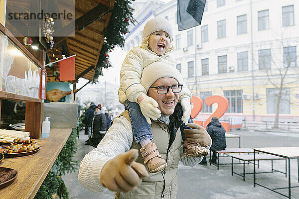 Fröhlicher Vater trägt Tochter am Marktstand in der Stadt