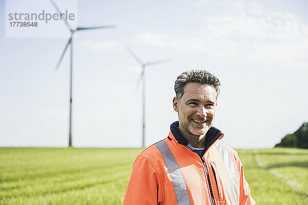 Lächelnder Ingenieur steht an einem sonnigen Tag im Feld