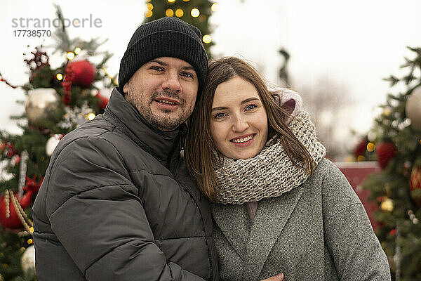 Lächelndes Paar in warmer Kleidung auf dem Weihnachtsmarkt