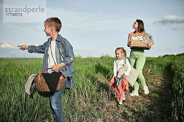 Junge mit Korb zeigt und geht mit Familie auf dem Feld