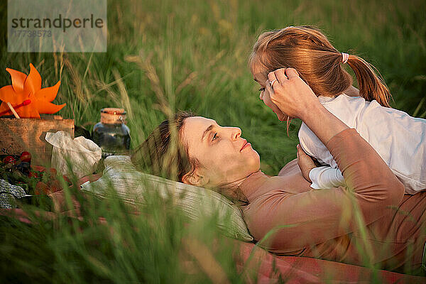 Mutter spricht mit Tochter  die im Gras liegt