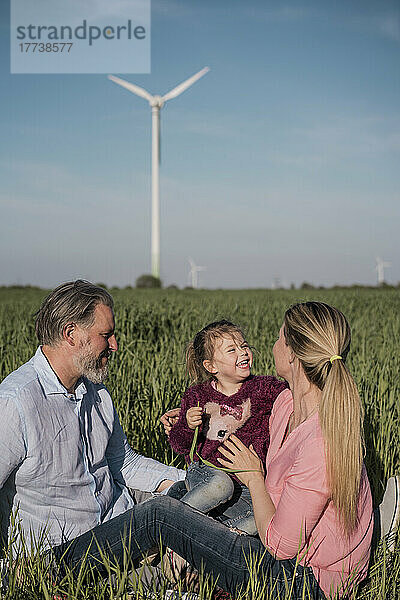 Glückliches Mädchen  das an einem sonnigen Tag mit seinen Eltern im Feld sitzt