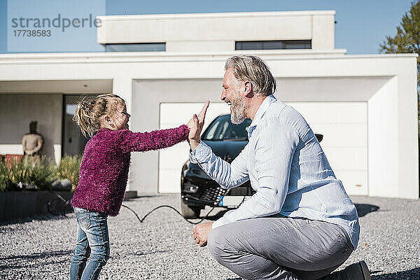 Glückliches Mädchen gibt seinem Vater an einem sonnigen Tag vor dem Auto High Five
