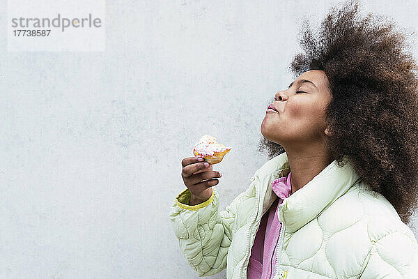 Mädchen mit geschlossenen Augen genießt es  Donut vor der Wand zu essen