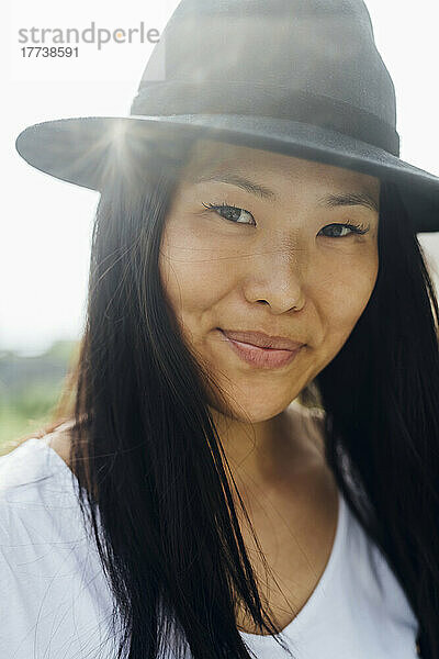 Smiling young woman with black hair wearing hat on sunny day