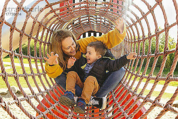 Glückliche Frau mit Sohn spielt im Klettergerüst auf dem Spielplatz