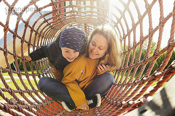 Glückliche Mutter und Sohn spielen im Klettergerüst auf dem Spielplatz