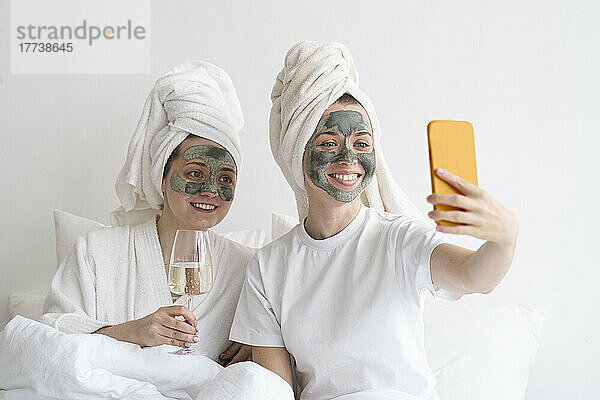 Fröhliche Freunde mit Gesichtsmasken machen Selfies mit dem Handy