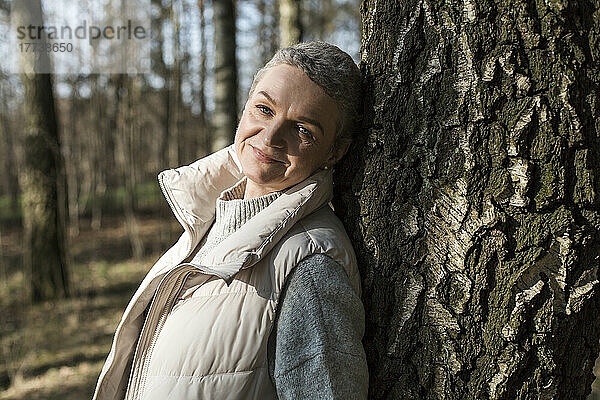 Porträt einer lächelnden Frau  die sich an einen Baumstamm lehnt