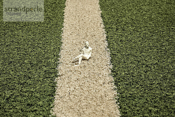 Kleine Figur liegt auf Kunstrasen des Fußballplatzes