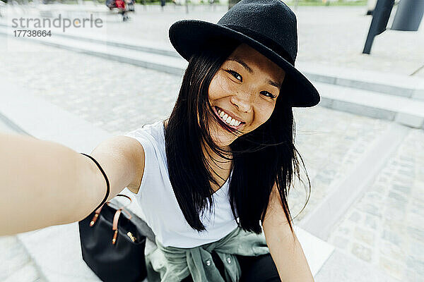 Happy woman with black hair wearing hat taking selfie