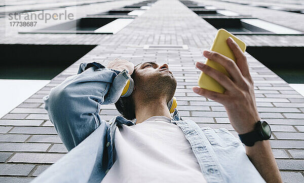 Mann hält Mobiltelefon und steht an Gebäudewand
